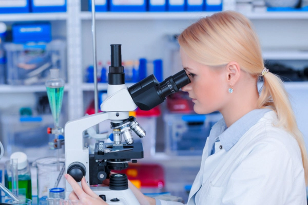 attractive young scientist looking at the microscope slide in the forensic laboratory