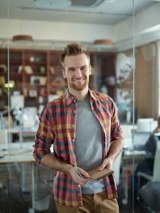 storyblocks portrait of cheerful handsome man wearing colorful checkered shirt smiling to camera standing by glass wall in modern office_BT7xL7T7bf 225x300